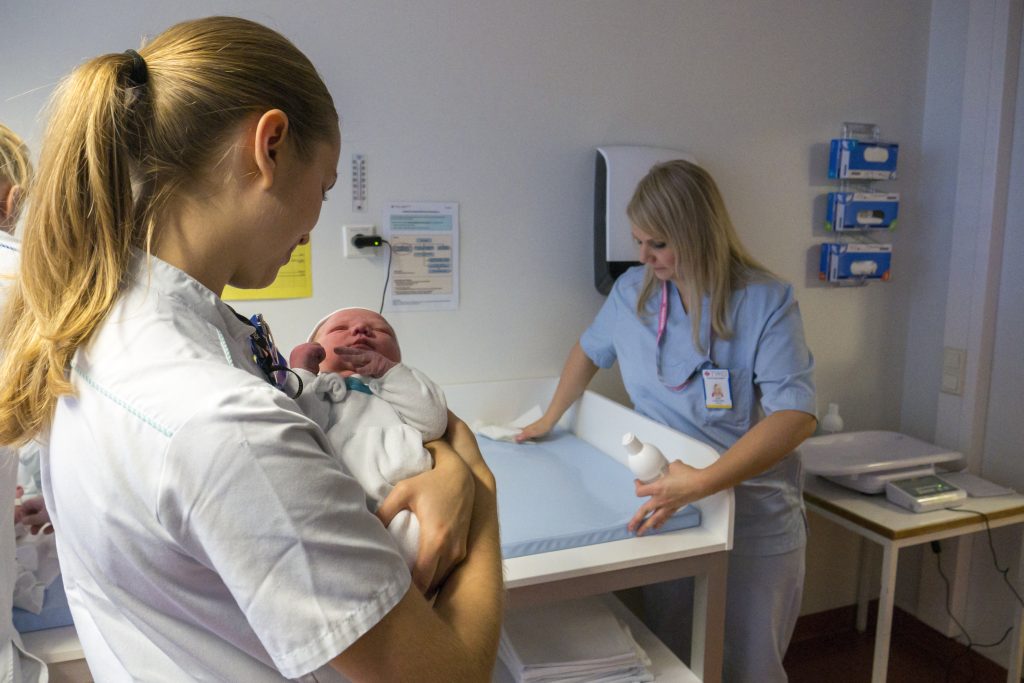 Kätilöopiskelija Johanna Tähkäpää pitelee vauvaa kun opiskelijavastaava Anni Uusitupa desinfioi hoitoalustaa.