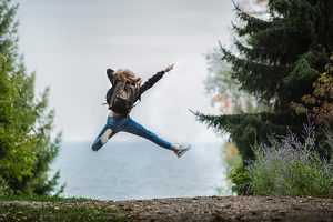 Iloinen opiskelija hyppää ilmaan metsäaukealla