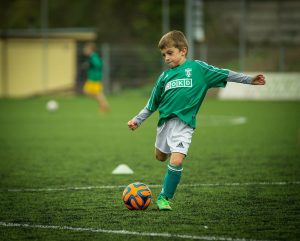 Kuvassa on nuori poika pelaamassa jalkapalloa.