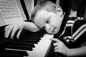 Kuvassa pieni pianisti nojaa pianon koskettimia vasten niin, että hänen poskensa on koskettimilla.