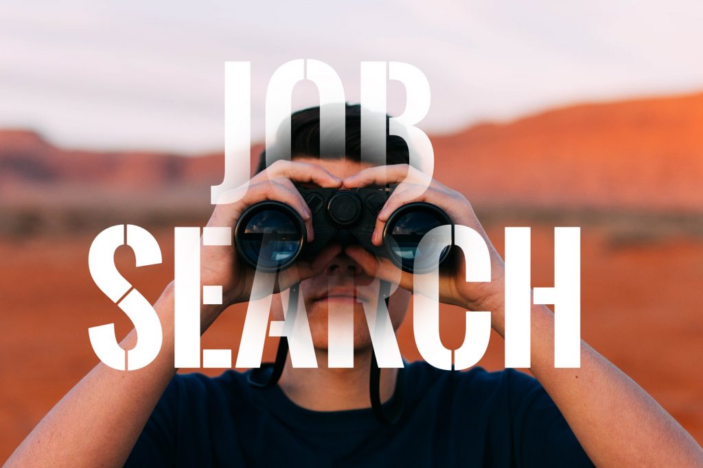 Kuvassa henkilö katselee kiikareiden läpi kohti kuvan katsojaa. Henkilön kohdalla lukee job search.