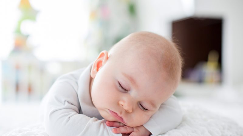 Kuvassa on vauva, joka on nukahtanut vatsallaan ollen, kädet posken alla.