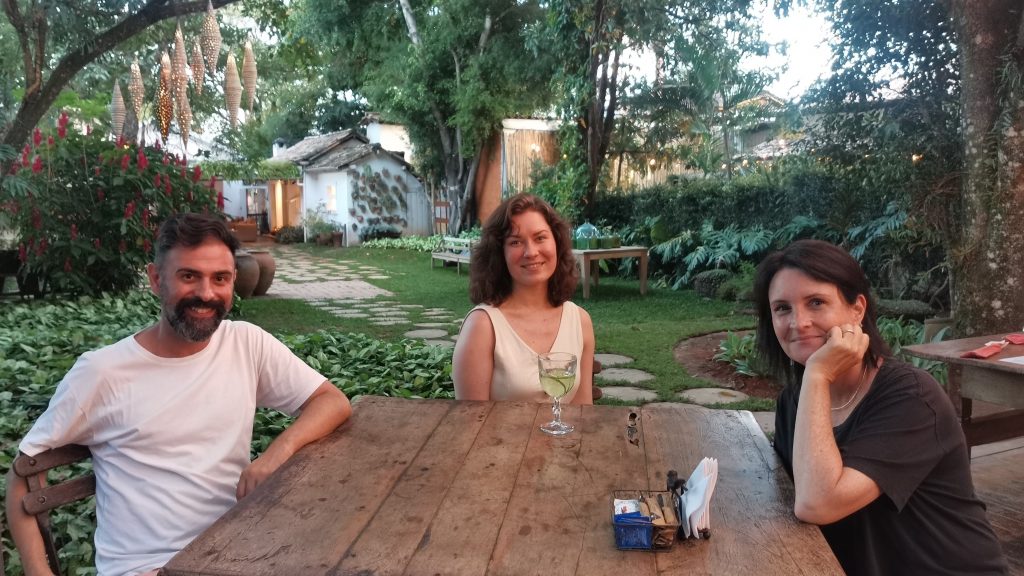 Kuvassa on kolme henkilöä puisen pöydän ympärillä puutarhassa.