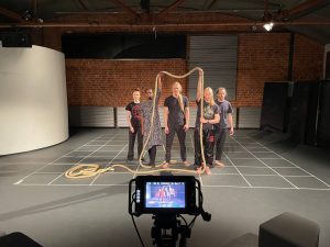 Kuvassa näkyy etualalla videokamera ja sen näytöllä kuva näyttämöstä, joka näkyy kuvan keskiosassa ja jolla on viisi henkilöä, joista kaksi pitelee köyttä keskellään olen henkilön pään yläpuolella.