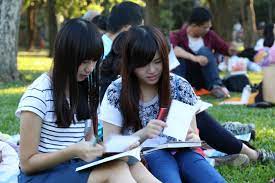 kaksi aasialasita tyttöä opiskelee nurmikolla istuen
