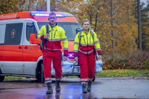 Kaksi ensihoitajaa kävelemässä tapaturmapaikalle, taustalla ambulanssi.