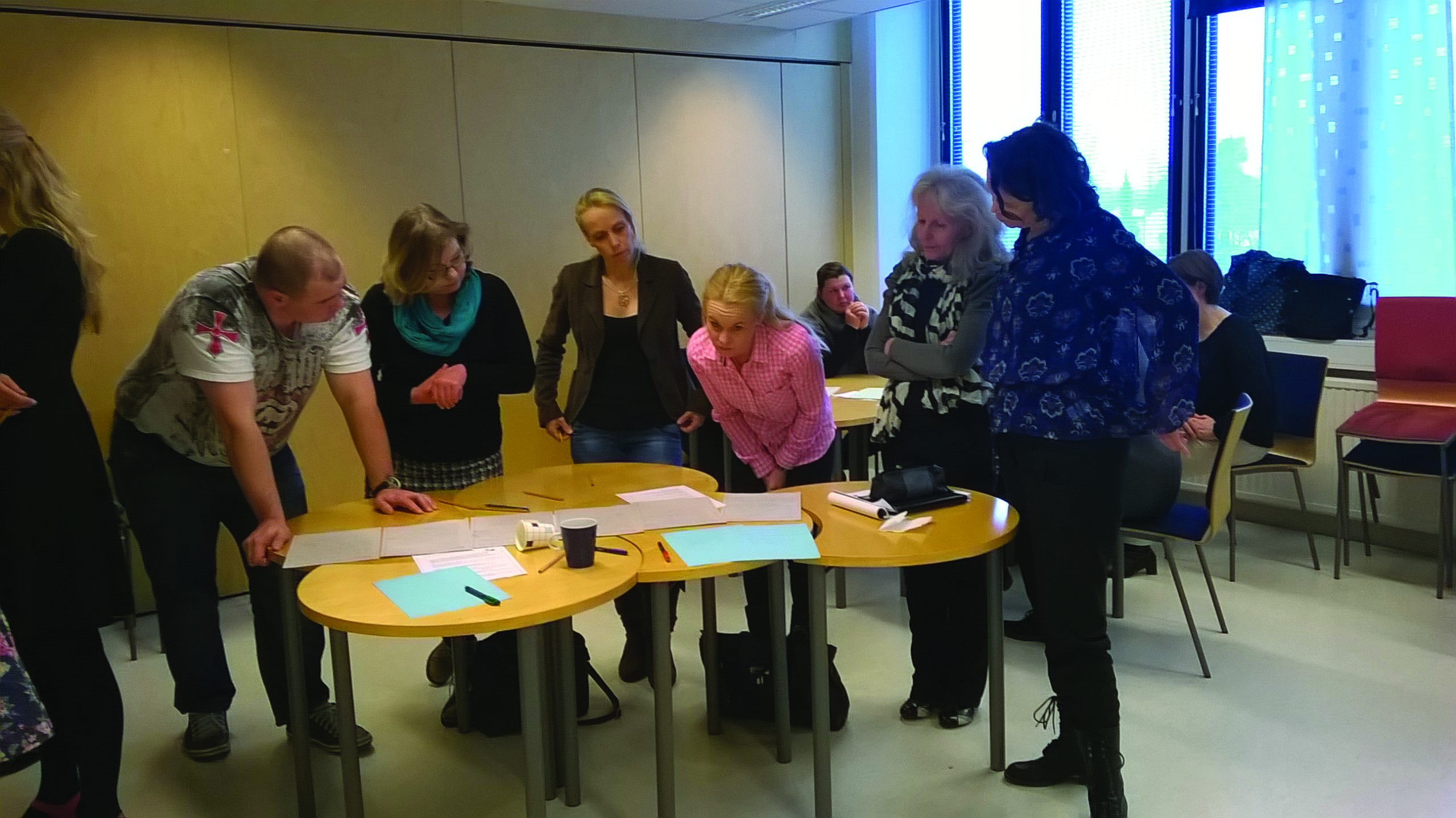 Six people have stooped down at the table to look at the papers.