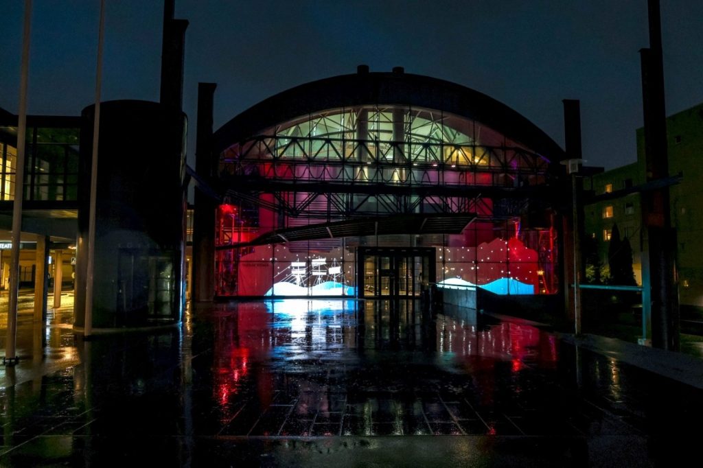 Kuvassa näkyy Taideakatemian Naruteatterin pääty valaistuna pimeässä illassa. Päädyn suurissa ikkunoissa näkyy projisointeja, jj. purjelaiva.