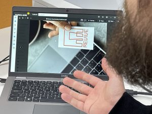 Kuvassa näkyy läppäri, jonka ruudulla on kuvakortti, jossa lukee Revive. Kuvassa näkyy myös avoin kämmen läppärin näppäimistön yllä.