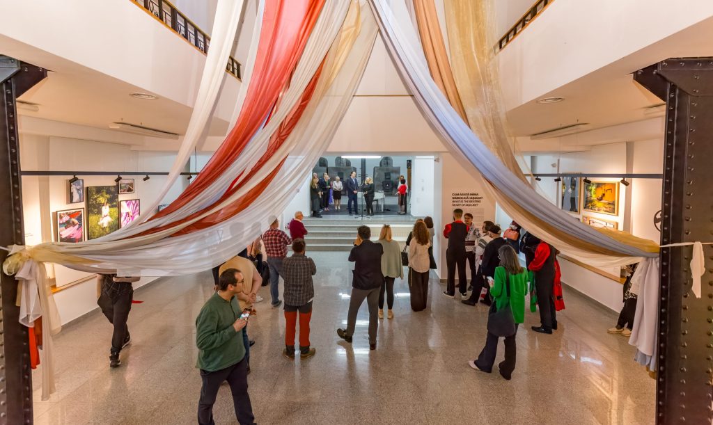 Kuvassa on galleriatila ylhäältä alaspäin kuvattuna. Ihmiset kiertelevät tilassa, jonka seinillä on teoksia.