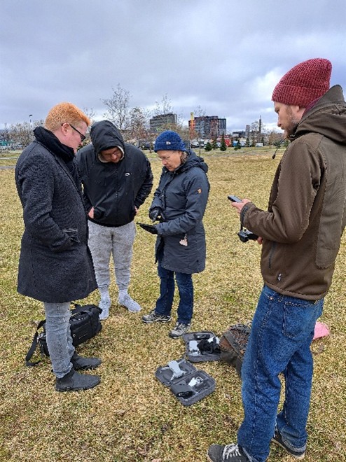Kuvassa on neljä ihmistä kumartuneena tutkimaan dronen lennättämiseen liittyviä laitteita.