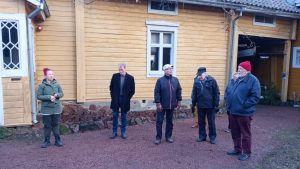 Ikämiehet museokierroksella: neljä miestä ja opas vanhan puutalon pihapiirissä