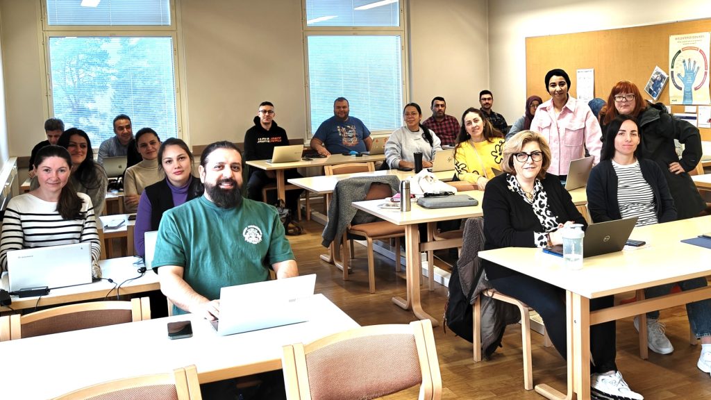 Monikulttuurinen opiskelijaryhmä istuu pulpeteissaan luokkahuoneessa Suomessa.