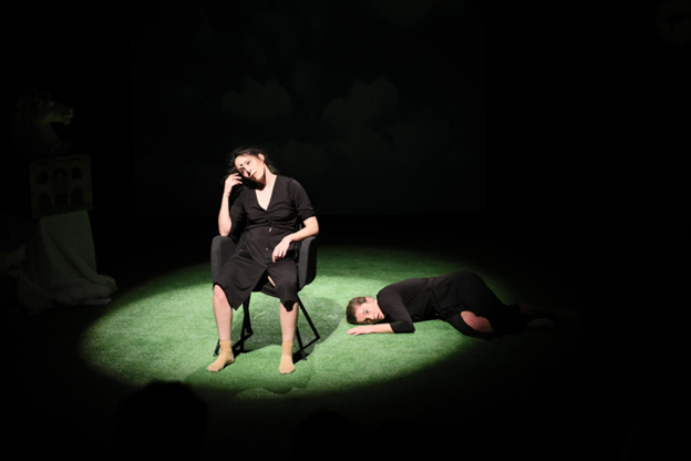 Näyttämöllä valokeilassa Paula Esteve ja Paula Segarra. Toinen istuu tuolissa käsi sivulle ääntyneen pään alla, toinen makaa kyljellään lattialla.