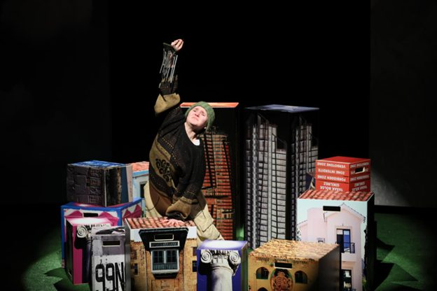 Salla Anttonen näyttämöllä laatikoista muodostuvien lavasteiden keskellä.