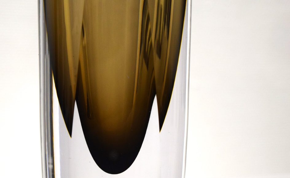 Kuvassa on yksityiskohta lasitaideteoksesta, väreinä ruskea ja kirkas lasi.