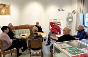 Ryhmä iäkkäitä ihmisiä muistelee entisajan esineitä museon salissa.