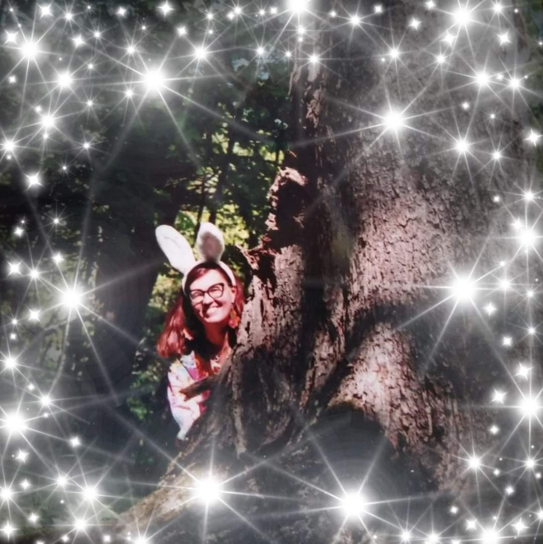 Nainen pupunkorvapanta päässään kurkkaa puun takaa, ympärillä tähtisade.