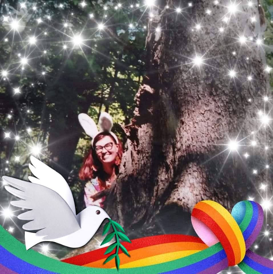 Nainen pupunkorvapanta päässään kurkkaa puun takaa, ympärillä tähtisade. Alareunassa kyyhky ja sateenkaariraidat.