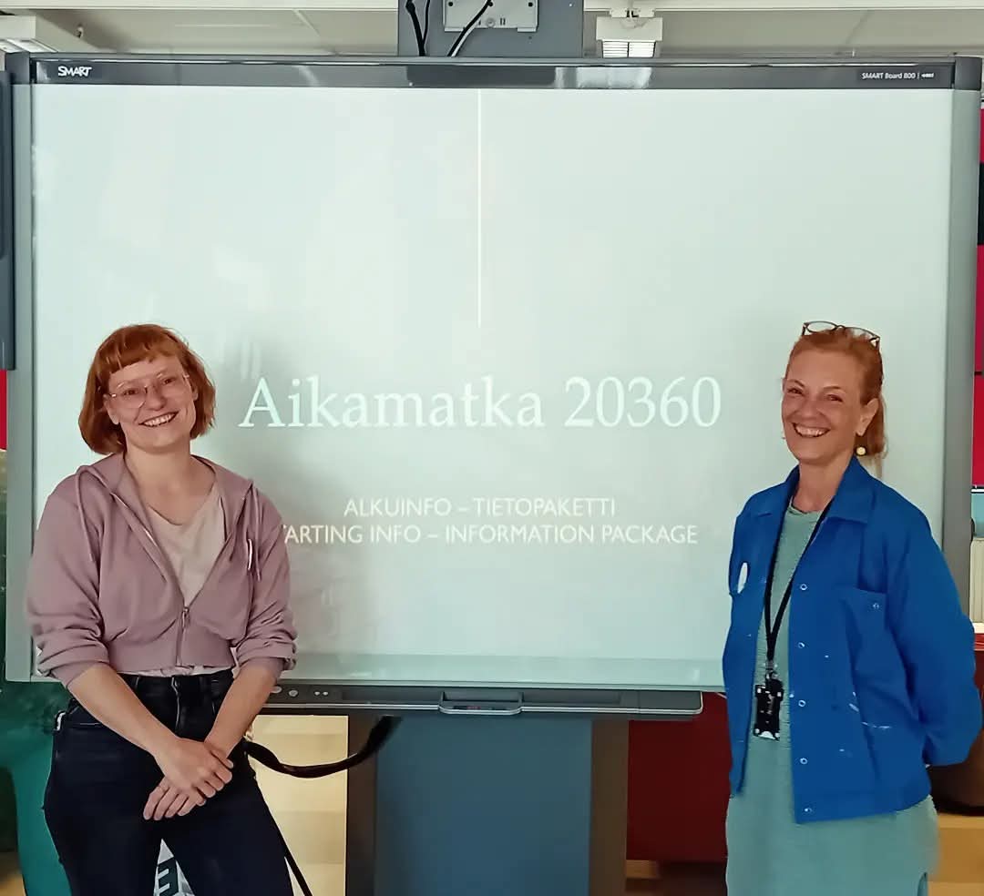 Kaksi naista seisovat ilmoituksen edessä. Ilmoituksessa lukee Aikamatka 20360.