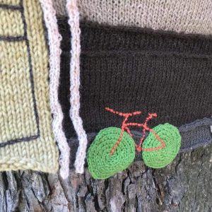 Näkyy pieni osa puusta, sen runkoon on kiinnitetty pyörää kuvaava virkkaus ja alla neulottu työ.