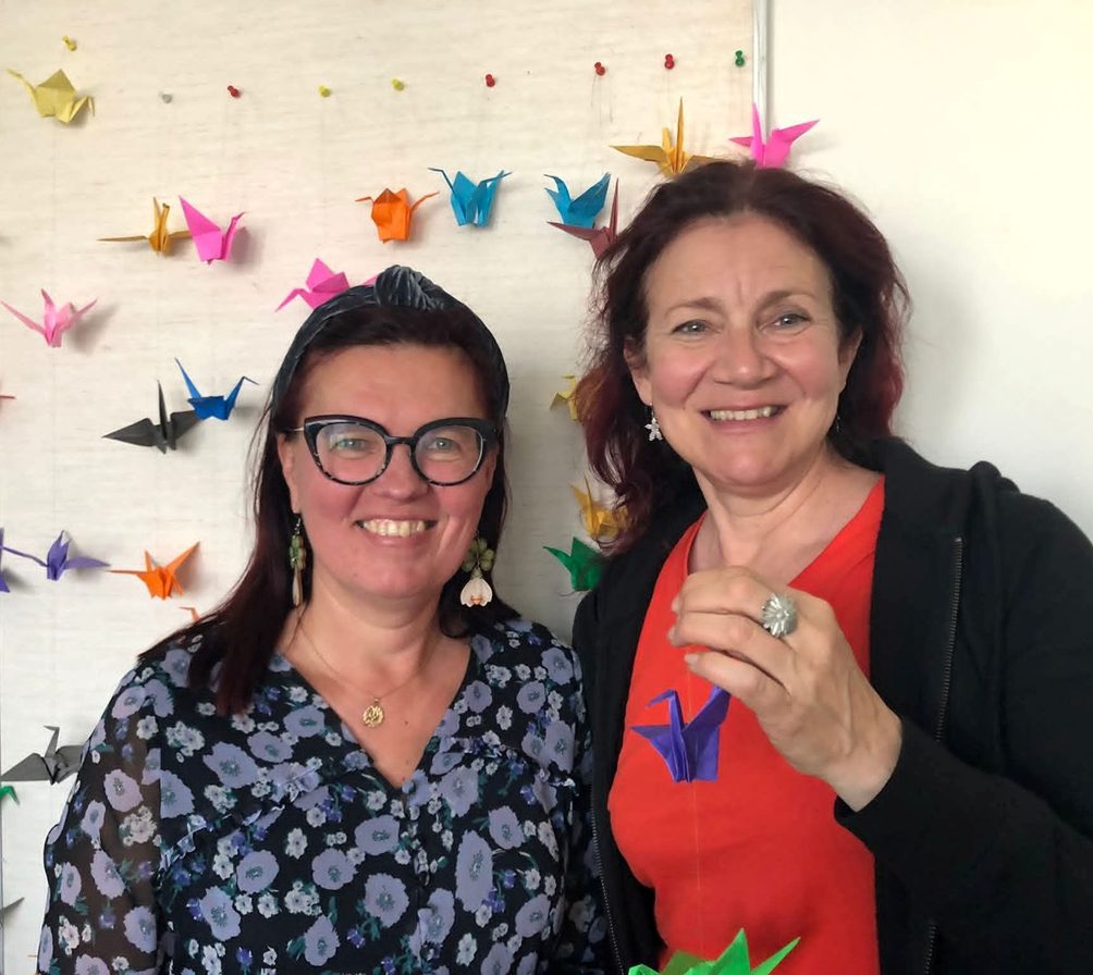 Kuvassa kaksi henkilöä, taustalla origameja.