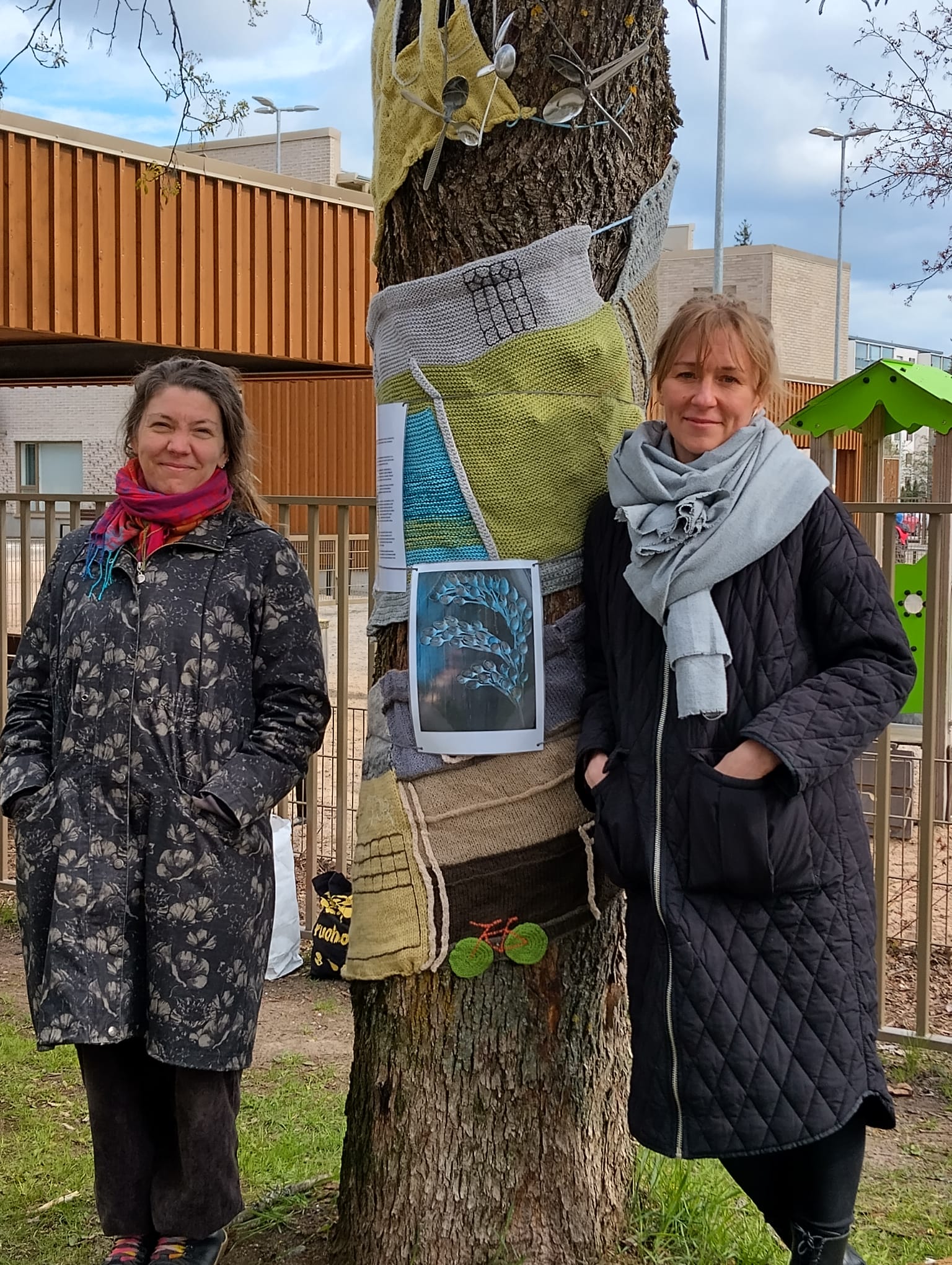 Kaksi henkilöä kankaalla verhotun puun vieressä.