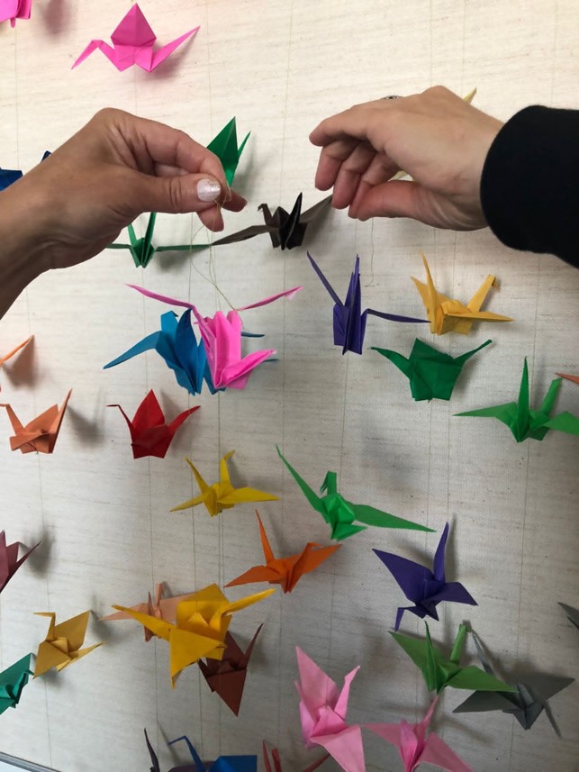 Kaksi ihmisen kädessä origameja, taustalla seinällä lisää.