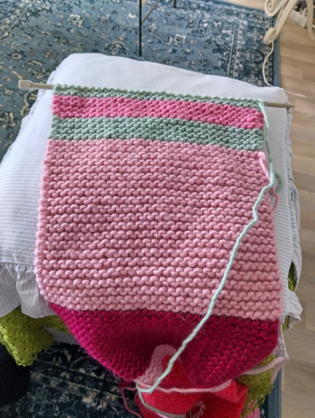 Keskeneräinen raitaneule tyynyn päällä lattialla.