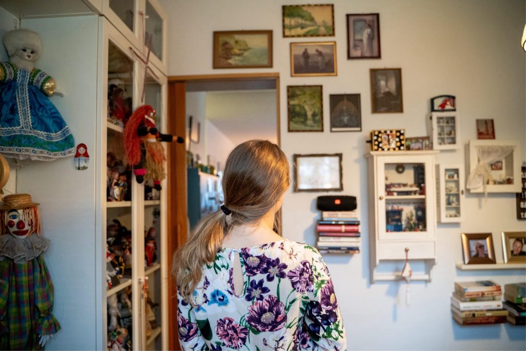 Kuvaaja on henkilön takana, ja kamera näyttää hänen selkänsä ja samalla hänet katselemassa yksityiskodin seinällä olevia kuvia.