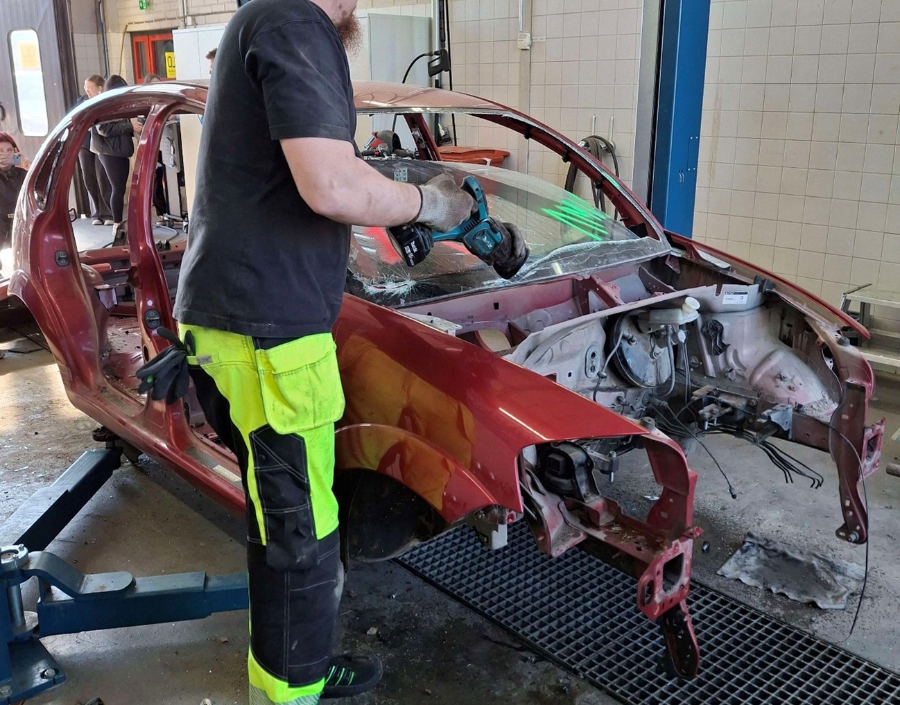 Henkilö leikkaa purettavan auton tuulilasia puukkosahalla.