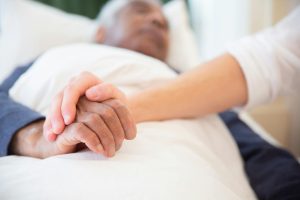 Potilas vuoteessa hoivatilanteessa. Lähikuvassa hoitajan ja potilaan kädet. Pexels