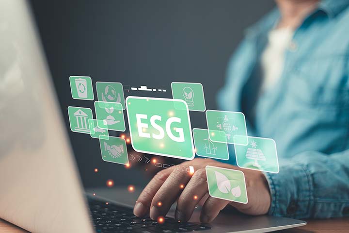 henkilö kirjoittaa tietokoneella, vain kädet näkyvät. Käsien yläpuolella vihreitä ikoneita, joista suurimmassa lukee vihreällä pohjalla ESG