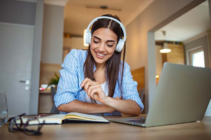 nainen opiskelemassa tietokoneella kuulokkeet korvilla