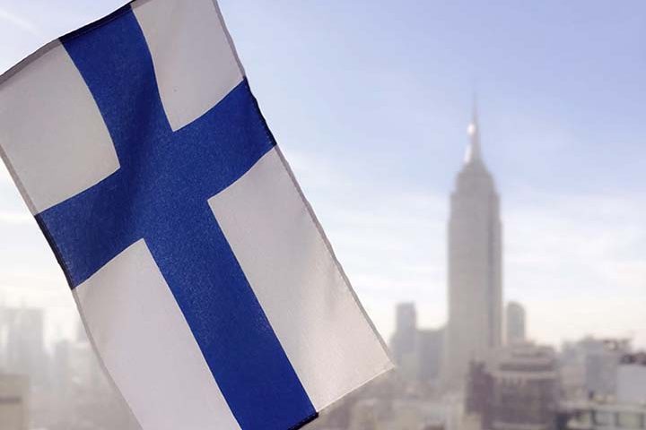 Etualalla Suomen lippu, taustalla pilvenpiirtäjä